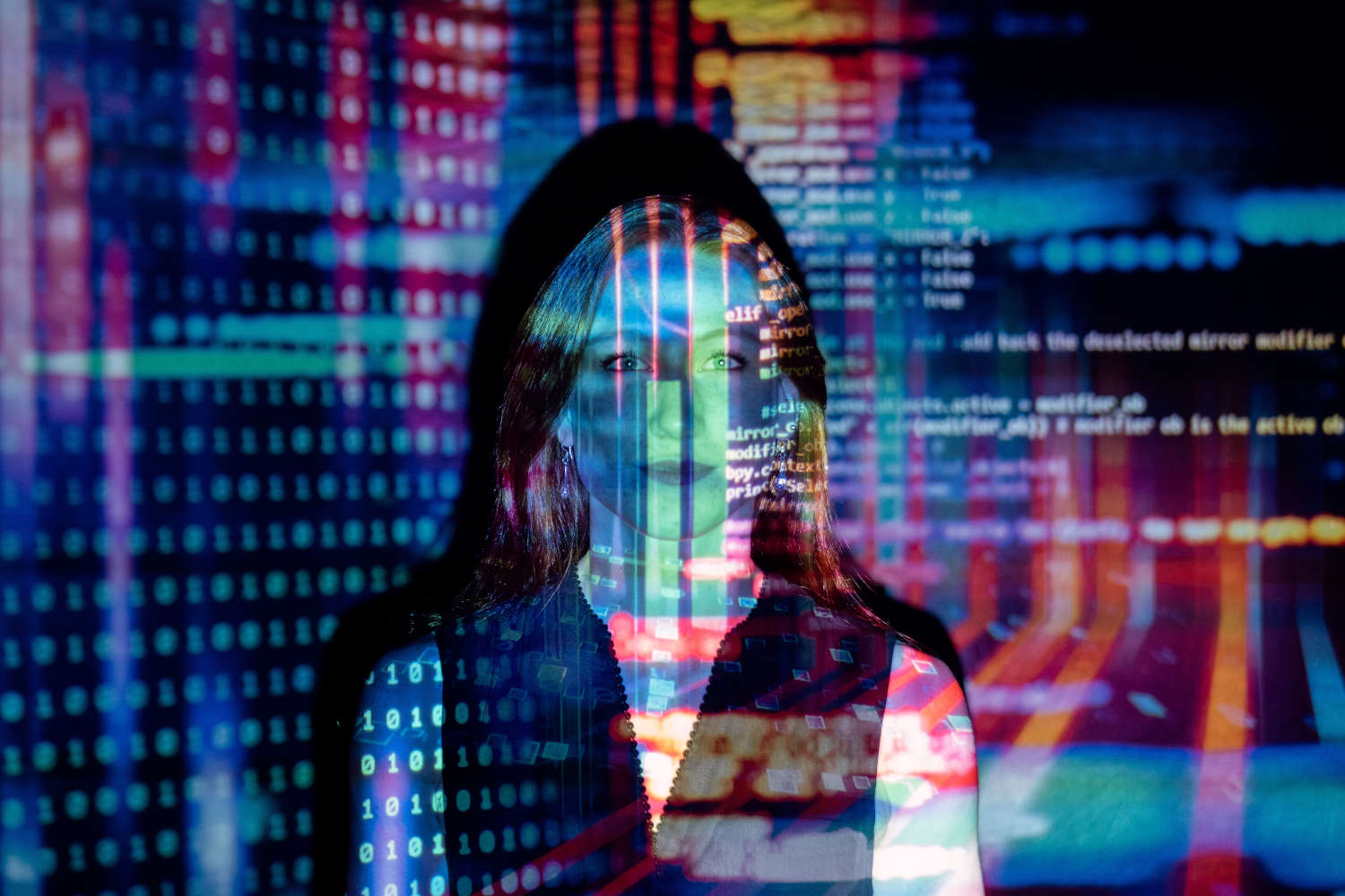 A woman looks into the camera while software code is projected over her.